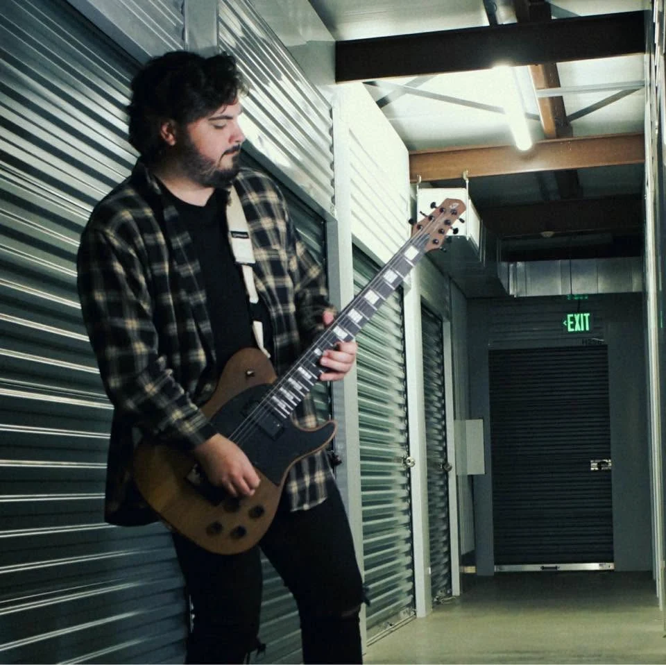 Tyler Ruehl with guitar in an industrial hallway