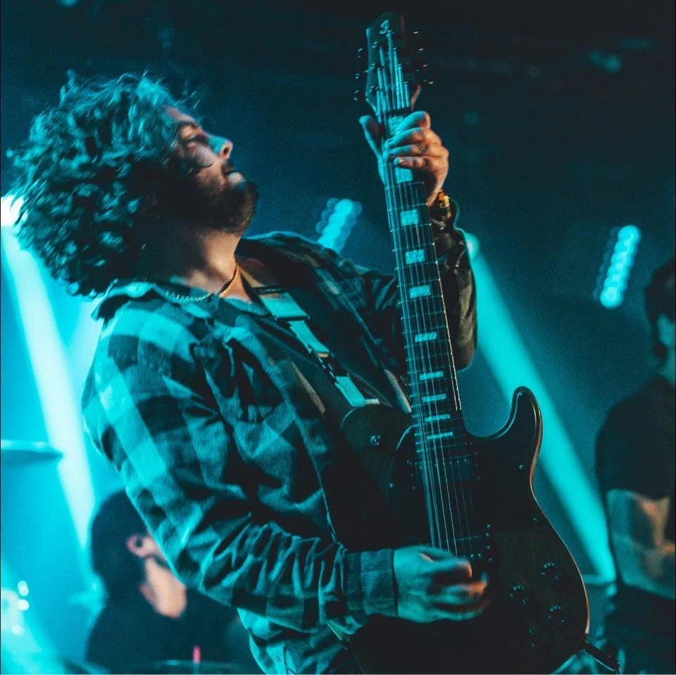 Tyler Ruehl performing guitar onstage under blue concert lights
